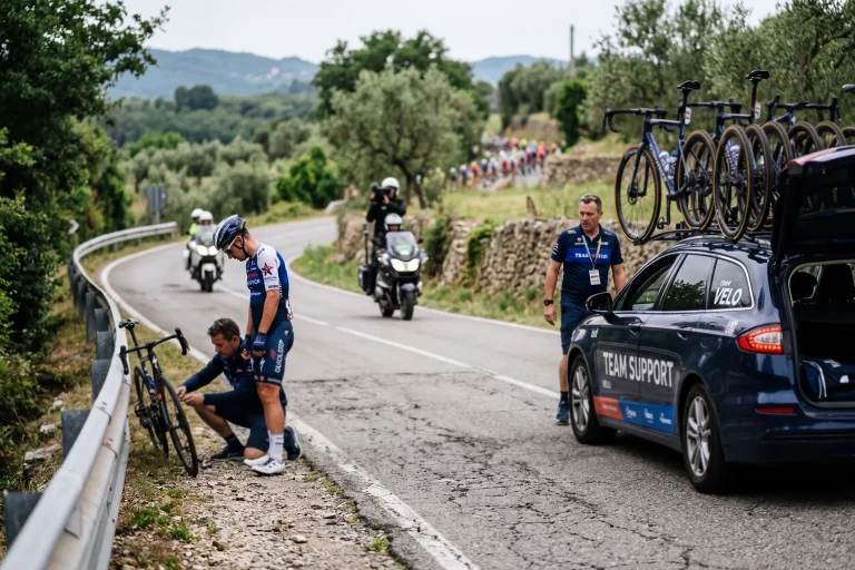 Ciclista retirándose de una carrera junto al coche del equipo