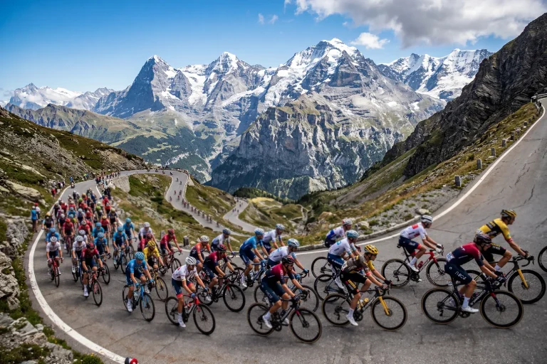 Pelotón de ciclistas ascendiendo un puerto de montaña con paisaje alpino